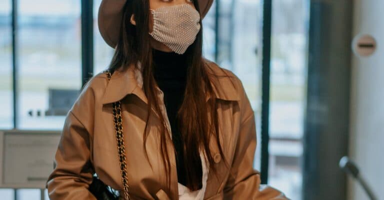 New York Blogs | Articles | News | Tips & Tricks | Video | FAQ | Information | Infograph. 21 A fashionable woman in a brown coat and hat wearing a face mask inside an airport lobby.