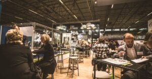 A bustling indoor business expo with professionals networking and engaging at various booths.