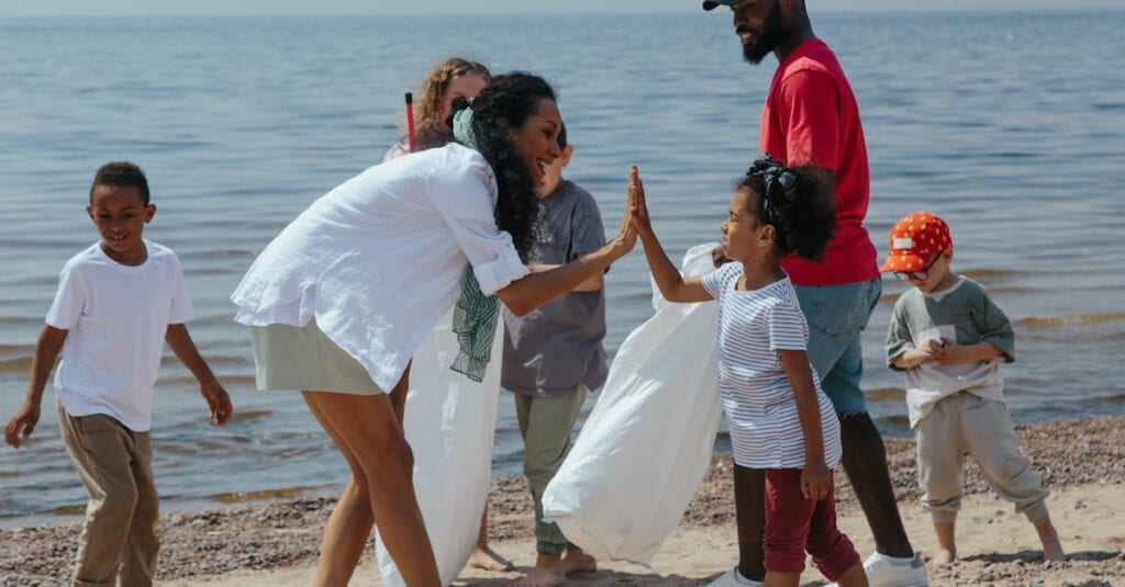 A diverse group of volunteers, including children and adults, clean up a beach and celebrate with high-fives.