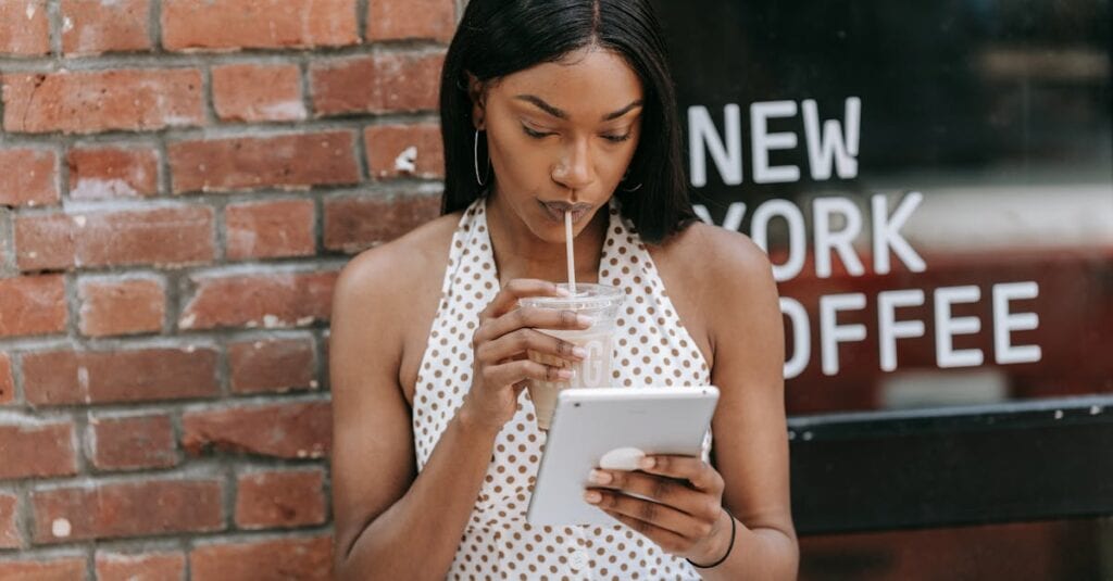 Woman sipping iced coffee and using a tablet outside a New York coffee shop.