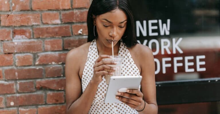 Woman sipping iced coffee and using a tablet outside a New York coffee shop.