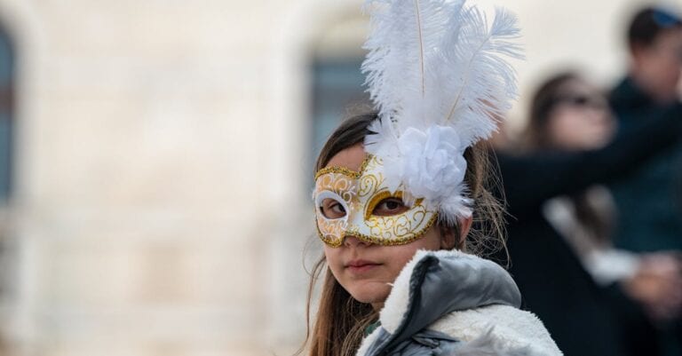 A child wearing a decorative gold and white mask with feathers at a festival.