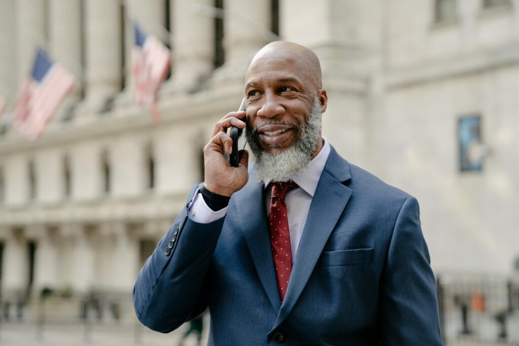 A mature businessman in a blue suit smiling during a phone call outside an iconic building.