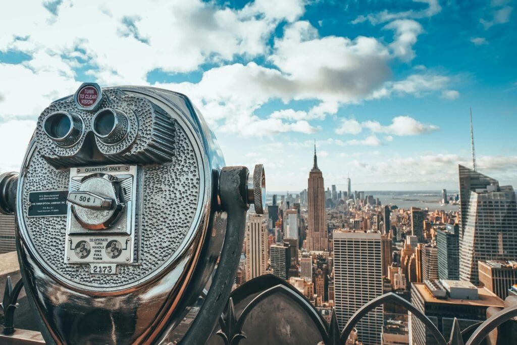 View of New York City skyline featuring iconic Empire State Building with observation binoculars in the foreground.