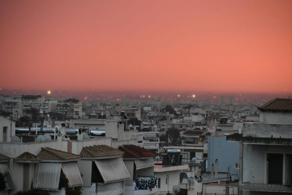Captivating view of Athens cityscape under a vibrant red sunset sky, showcasing urban architecture.