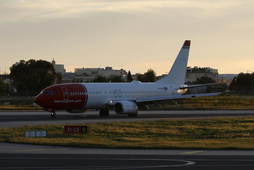 A Norwegian airplane on a runway during sunset, ready for takeoff.