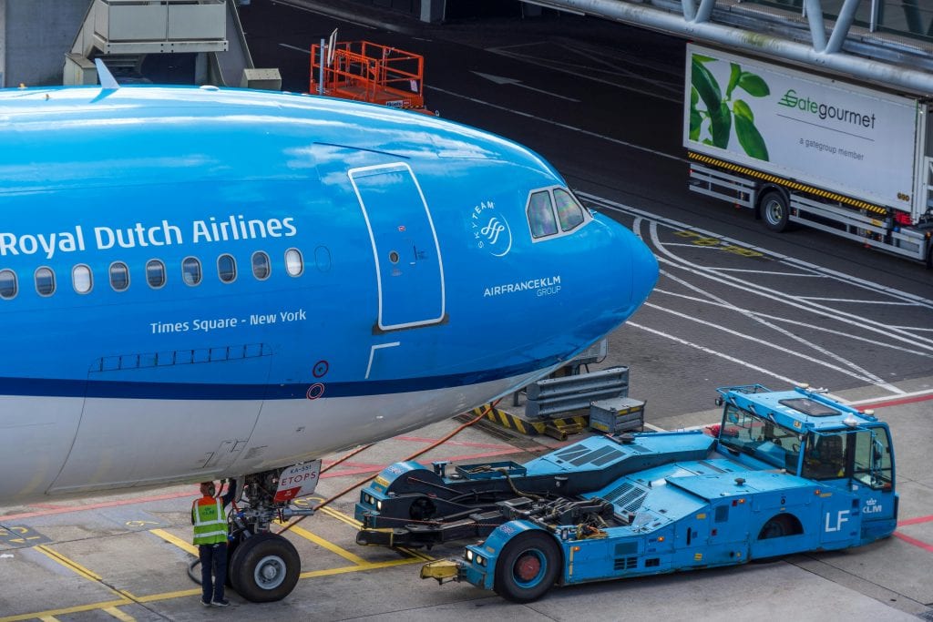 Close-up of Royal Dutch Airlines plane being serviced at airport with cargo vehicles.