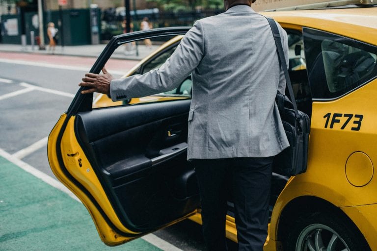 Back view crop unrecognizable African American male in formal outfit opening taxi door on modern city street