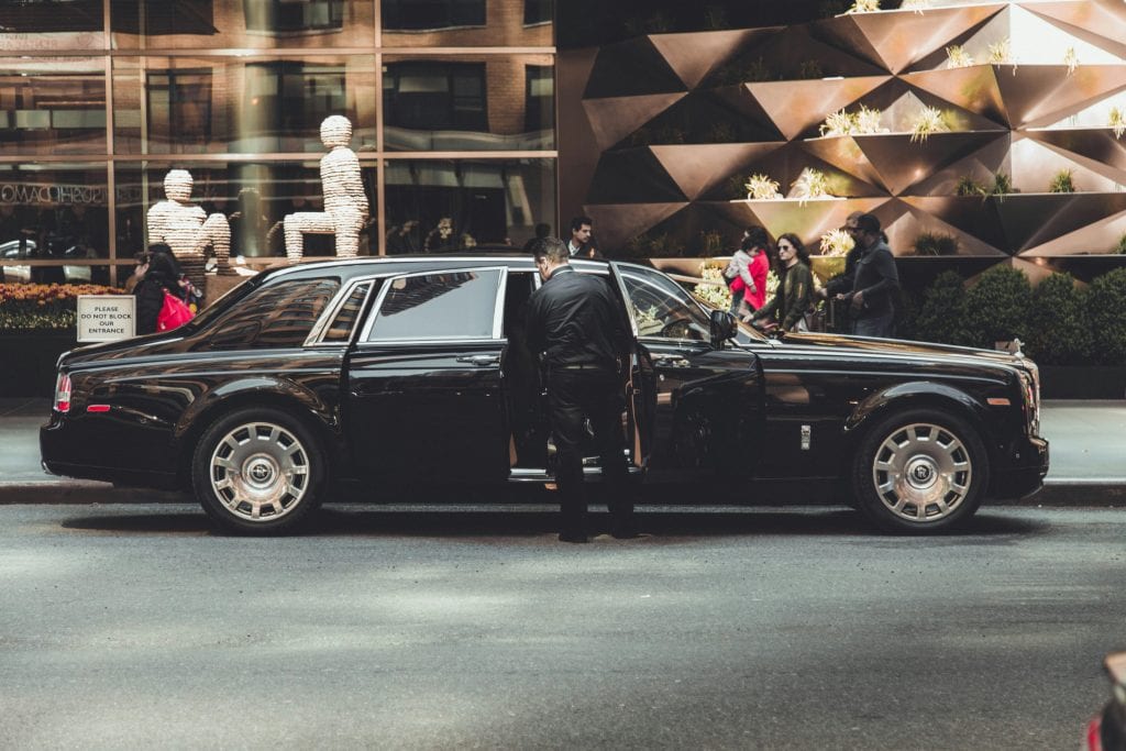 Elegant Rolls Royce with chauffeur outside modern building in New York City, illustrating luxury and class.