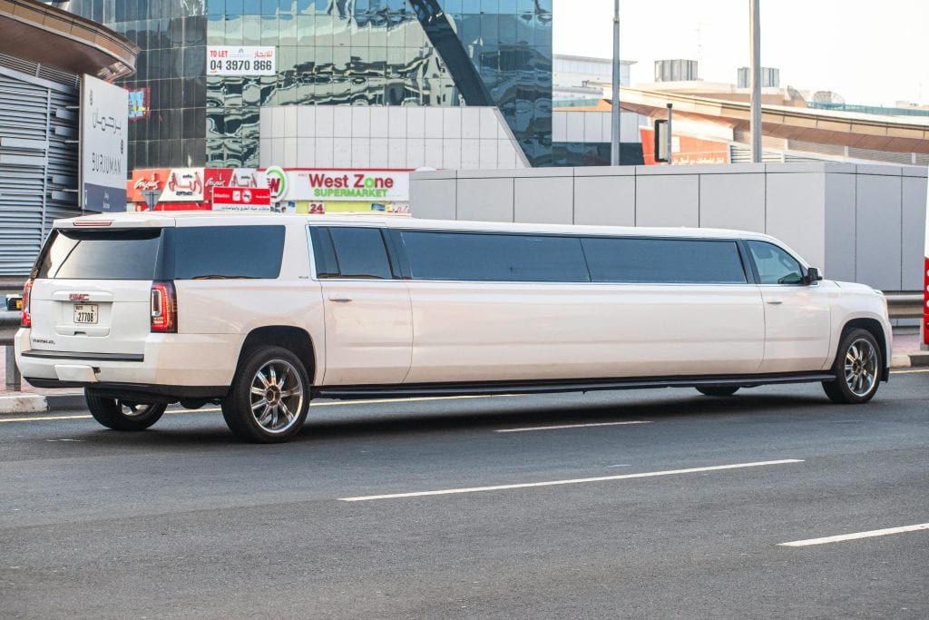 White GMC Yukon XL limousine parked on a bustling city street during the day.