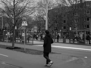 Black and white street view of Amsterdam featuring a pedestrian near a public transportation stop.