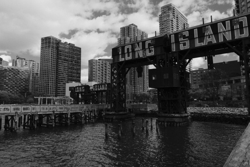 Dramatic black and white view of Long Island City waterfront with iconic signage.