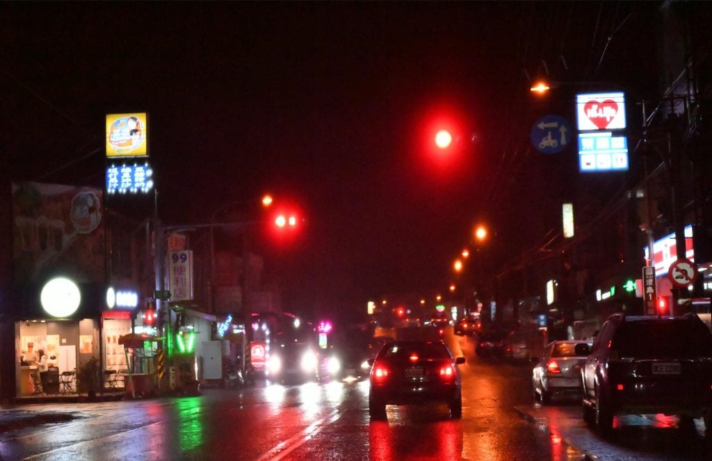 Urban street at night with vibrant neon signs and cars in the rain.