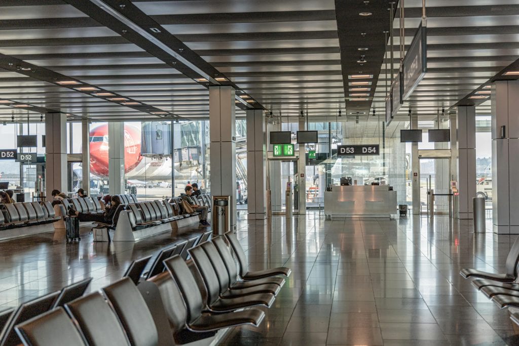 Spacious airport terminal with empty seating and a view of an airplane through large glass windows.