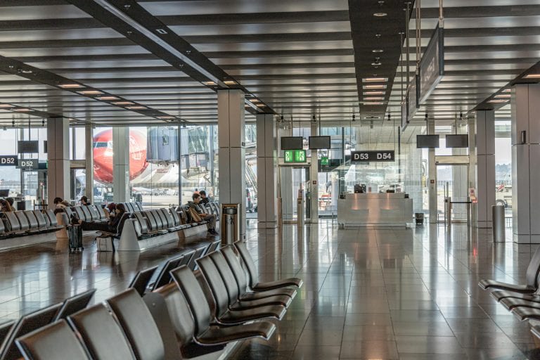 Spacious airport terminal with empty seating and a view of an airplane through large glass windows.