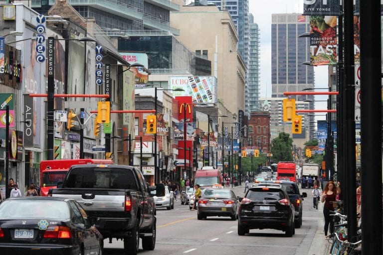 A bustling street scene of Yonge Street in downtown Toronto, filled with vehicles and pedestrians.