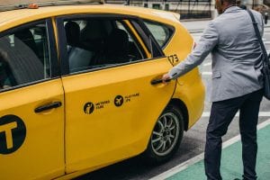An urban businessman opens a yellow taxi door on a busy city street, showcasing modern commuting.