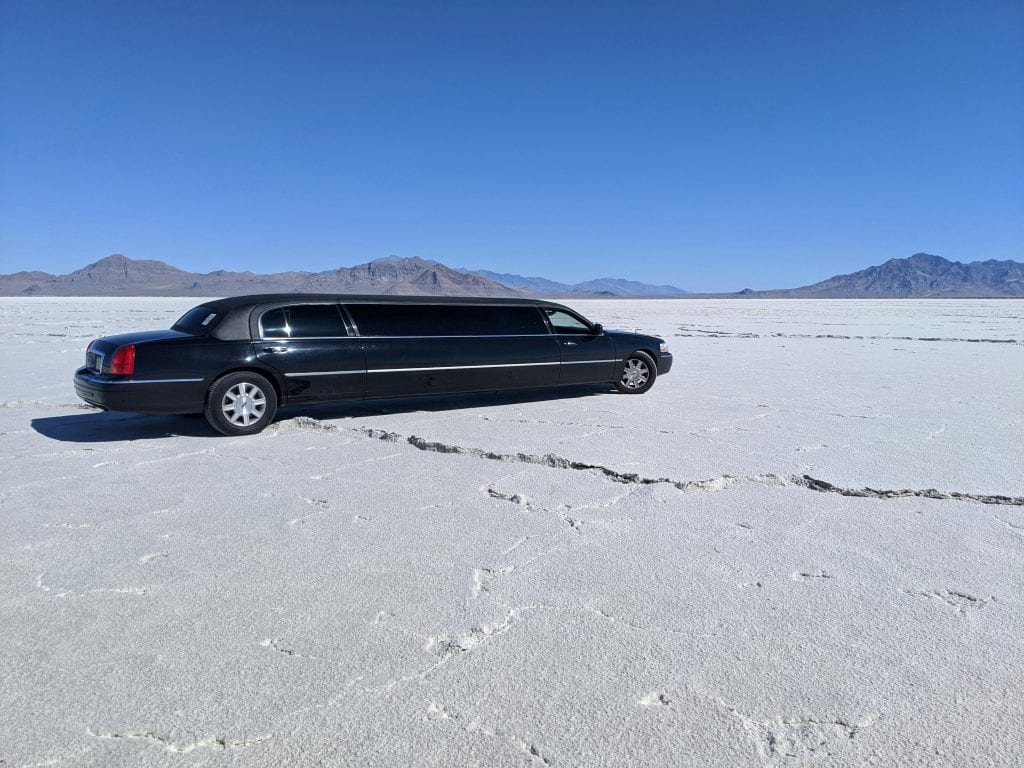 A sleek black limousine parked in a vast, dry desert with a clear blue sky.