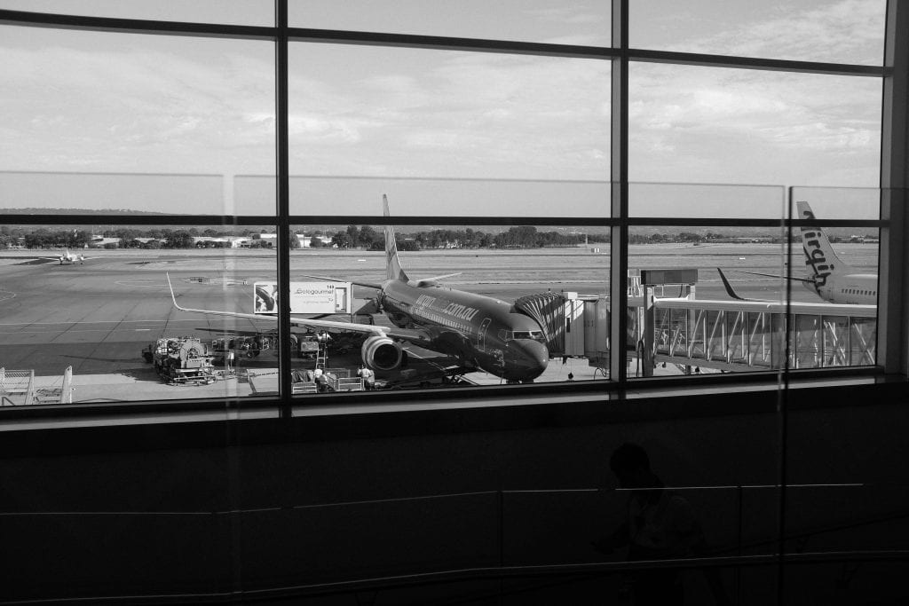 Monochrome view of an airport runway showcasing airplanes and gates through large windows.