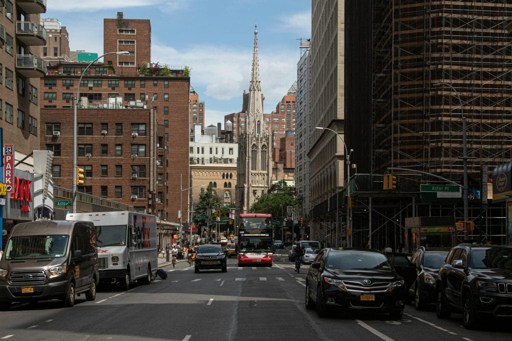 Vibrant cityscape of a New York street with traffic and historic church spire in the heart of downtown.