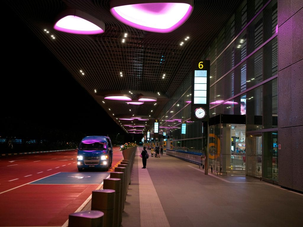 Night view of Singapore's Changi Airport entrance with illuminated canopy and bus.