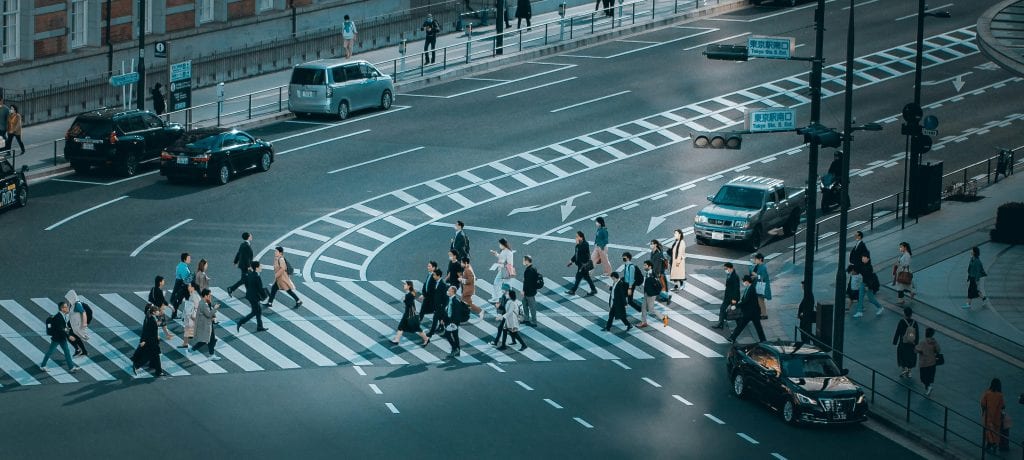 Aerial view of a busy pedestrian crossing in Tokyo, Japan, with cars and people under clear daylight.