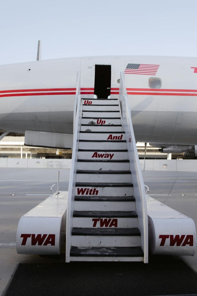 Vintage TWA airplane stairs with US flag at New York airport, showcasing retro airline travel.