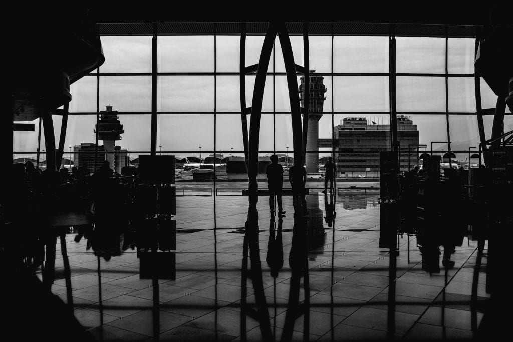 Black and white image of travelers silhouetted against large airport windows, capturing urban travel ambiance.