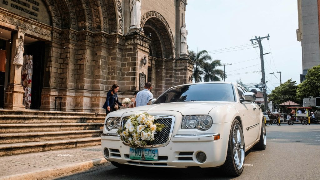 A luxurious wedding car with a floral bouquet parked outside a historic church entrance.
