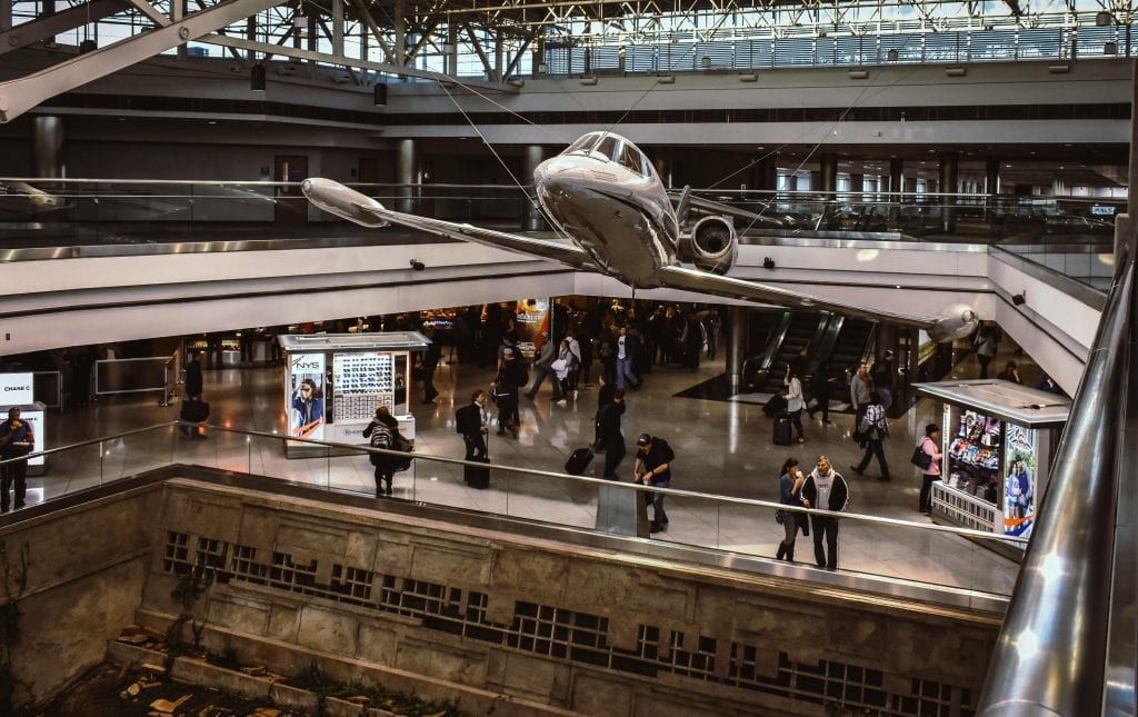 Inside a bustling airport with a hanging airplane and busy travelers.