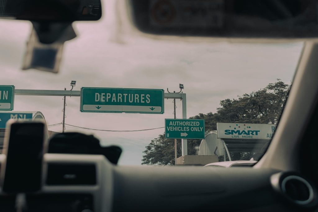View through windshield of car driving towards airport departure signs and authorized vehicle only lane, captured in soft daylight.