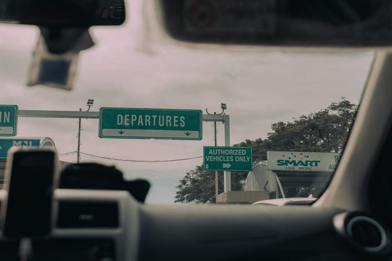 View through windshield of car driving towards airport departure signs and authorized vehicle only lane, captured in soft daylight.