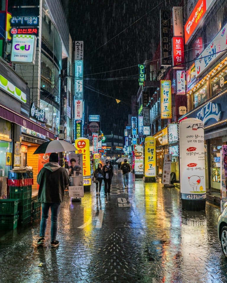 New York Blogs | Articles | News | Tips & Tricks | Video | FAQ | Information | Infograph. 49 Colorful neon-lit street in Seoul, South Korea showing bustling nightlife with reflections on wet pavement.