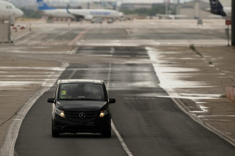 A black van driving on a rainy airport runway in Madrid, Spain, with planes visible in the background.