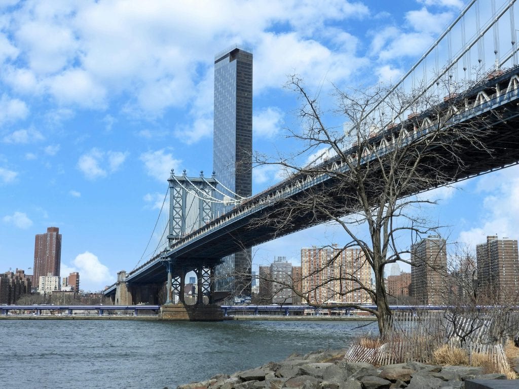 A scenic view of the Manhattan Bridge in New York City during winter, under a bright blue sky.