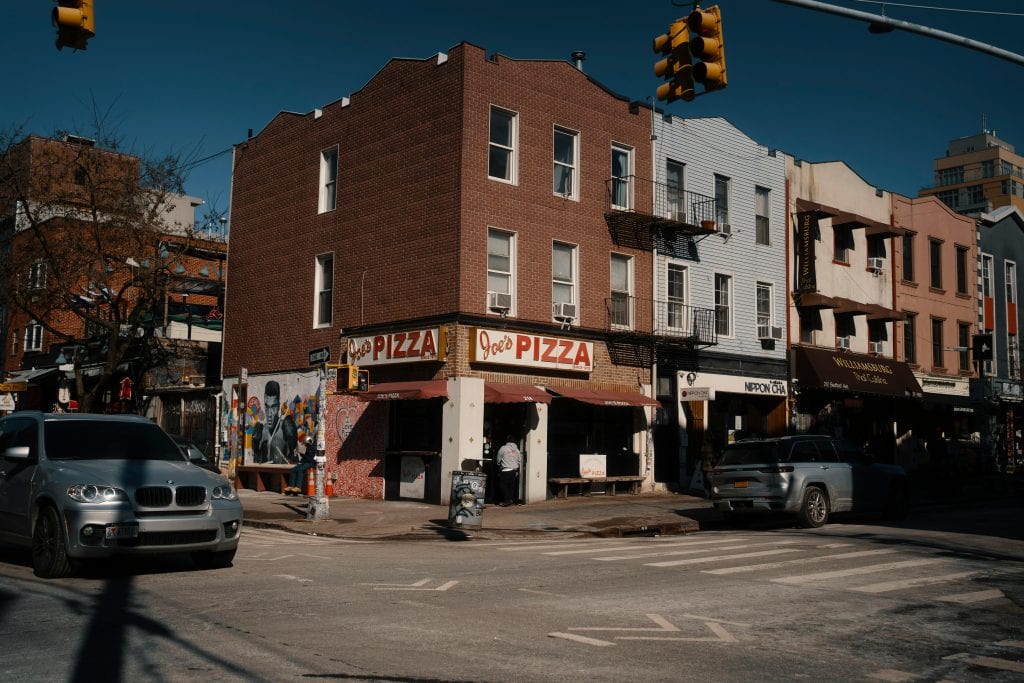 Street view of Joe's Pizza on a sunny day in Brooklyn, showcasing the lively urban atmosphere.