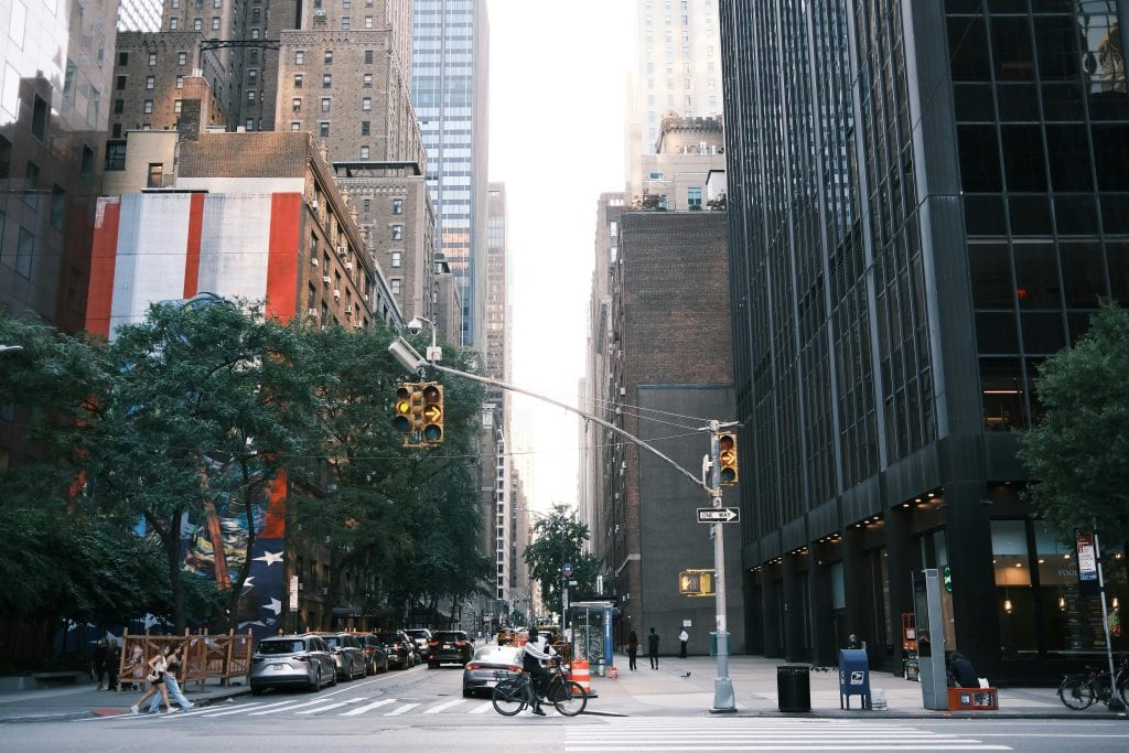 Busy city street with pedestrians and cyclists surrounded by towering buildings and traffic lights.