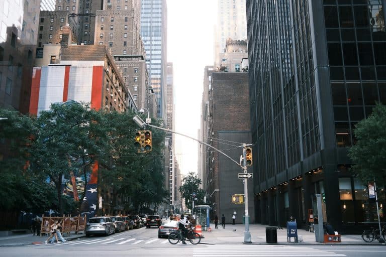 Car Service Blogs | Articles | News | Tips & Tricks | Video | FAQ | Information | Infograph. 6 Busy city street with pedestrians and cyclists surrounded by towering buildings and traffic lights.