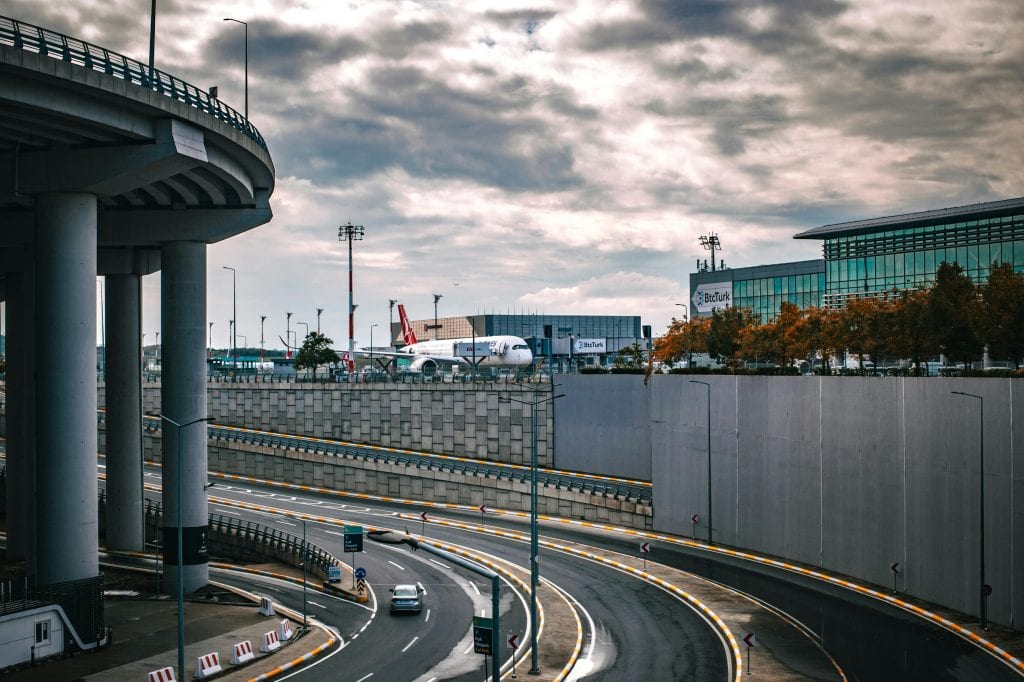 Urban scene featuring a busy airport terminal with an airplane and a highway under a cloudy sky.