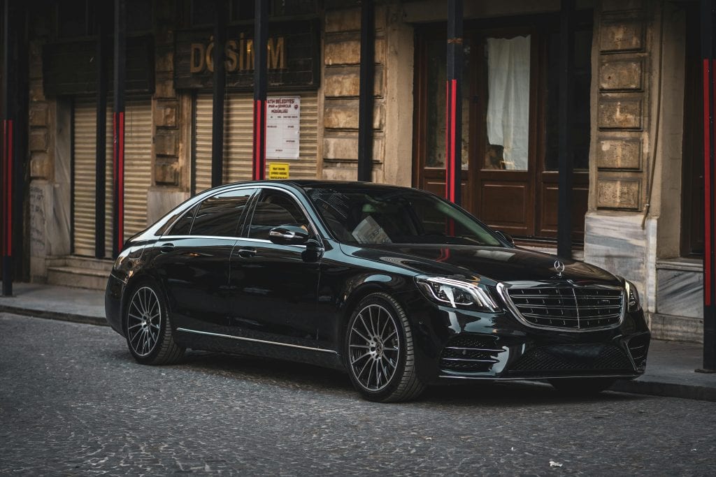 Sleek black luxury sedan parked on a cobblestone street in a historic European city.