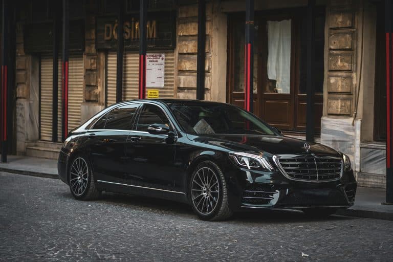 Sleek black luxury sedan parked on a cobblestone street in a historic European city.