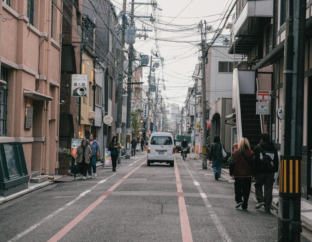 Lively street scene in Japan showing people walking and vehicles navigating a narrow city street.