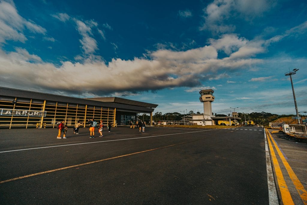 A small airport terminal with people walking on the tarmac under a blue sky.