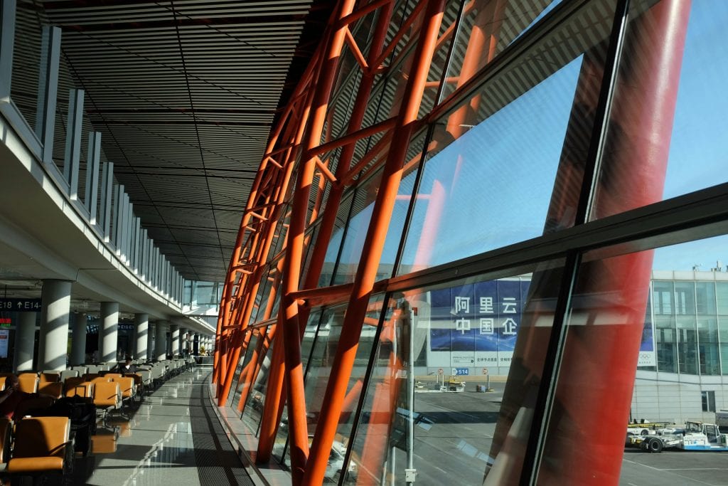 Large airport terminal with unique orange steel beams and expansive glass windows showcasing a bright day.