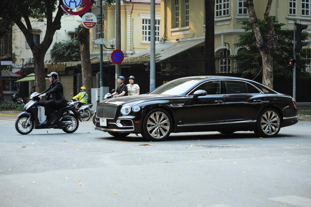 A luxury car and motorbikes wait at a city intersection, capturing urban street life.