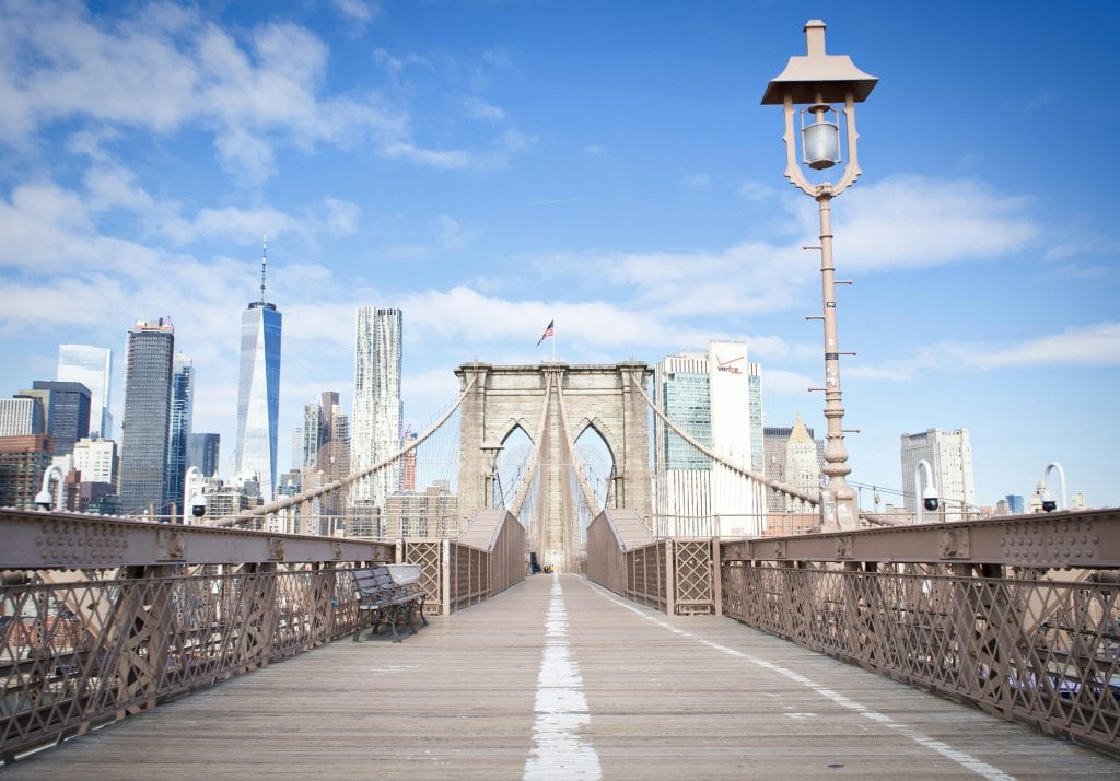 Wide-angle view of the Brooklyn Bridge leading to New York City's iconic skyline under blue skies.
