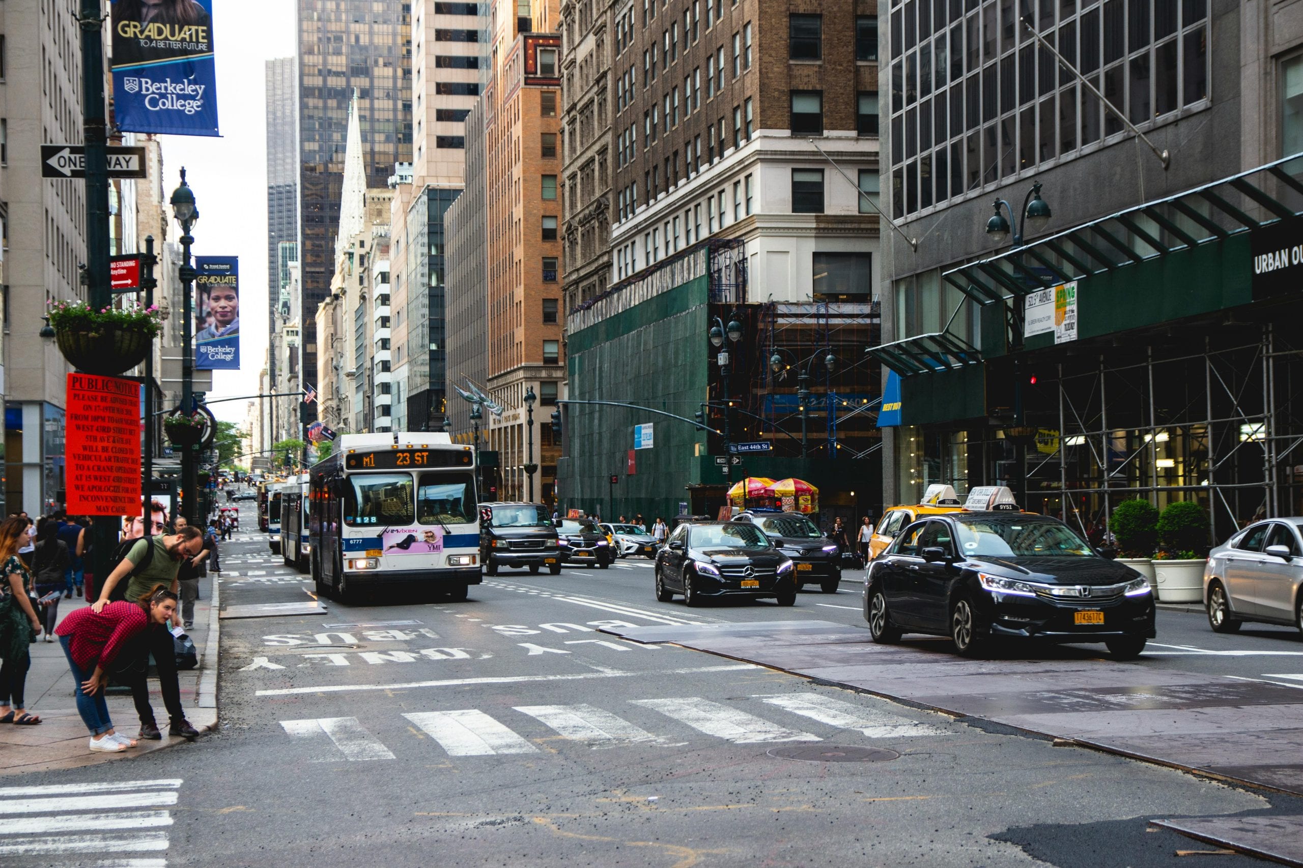 A vibrant New York City street scene with traffic, skyscrapers, and pedestrians crossing.