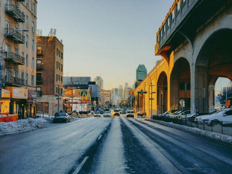 City street view with vehicles, buildings, and bridge during sunset in winter.
