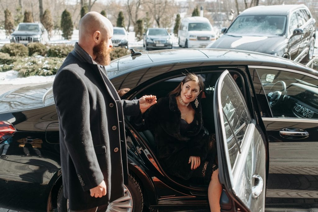 Stylish couple stepping out of a luxury black car, emphasizing elegance and sophistication.