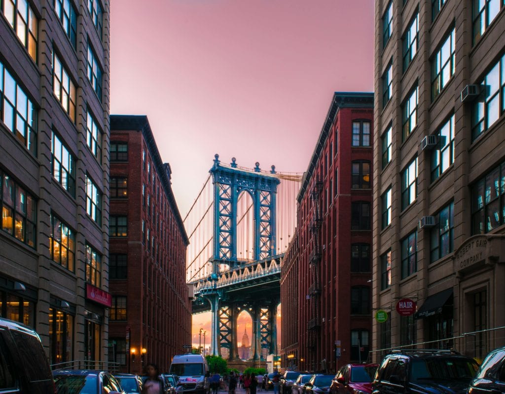 A stunning view of the Manhattan Bridge framed by city buildings at sunset in New York City.